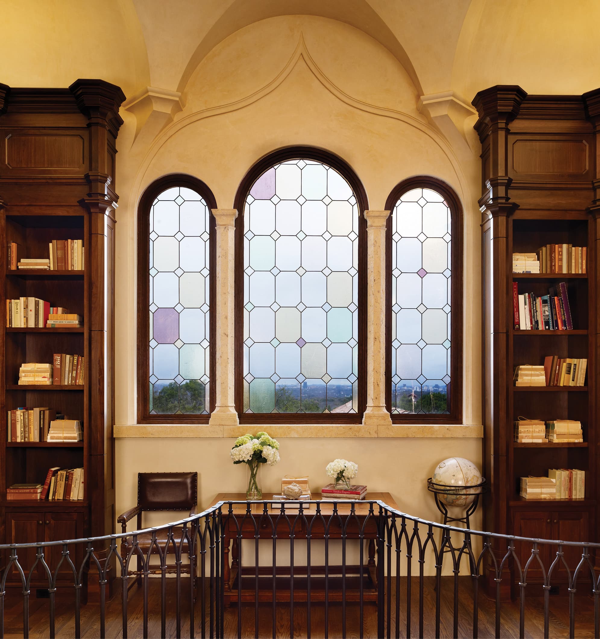 Arched stained glass windows flanked by wooden bookshelves